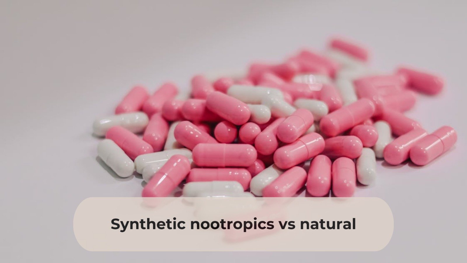 A pile of pink and white capsules scattered on a light surface with a beige text box overlay at the bottom reading “Synthetic nootropics vs natural.”